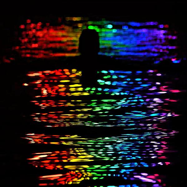 Man swimming at night in rainbow neon reflections at Penzance Lido